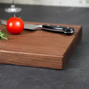 Detailaufnahme der natürlichen Holzmaserung und der elegant gefasten Kante eines handgefertigten Schneidebrettes aus amerikanischem Nussbaum