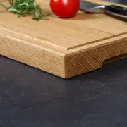 Detailaufnahme der natürlichen Holzmaserung und der elegant gefasten Kante eines handgefertigten Schneidebrettes aus Eiche - inkl. Saftrille und Griffmulde